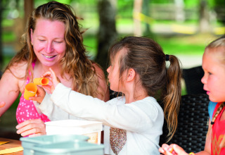Een vrouw en twee kinderen doen buiten knutselwerkjes op Camping Le Pech Charmant in Nouvelle-Aquitaine, Frankrijk.