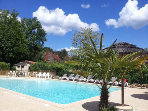 Piscina con tumbonas y palmeras en Camping Le Pech Charmant, parque de vacaciones en Nouvelle-Aquitaine, Francia.
