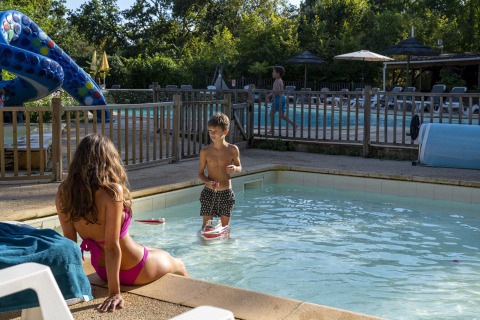 Mujer y niño disfrutan junto a la piscina infantil en Camping Le Pech Charmant, un parque vacacional en Francia.