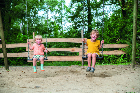 Dos niños se balancean felices en arenero en Camping Le Pech Charmant, Nouvelle-Aquitaine, Francia.