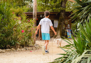 Jongen wandelt met hond langs grindpad tussen groen op Camping Le Pech Charmant, Frankrijk.