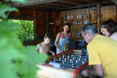 Familia juega futbolín en una cabaña con libros en Camping Le Pech Charmant, Nouvelle-Aquitaine.