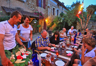 Vrolijke groep genietend van buiteneten op Camping Le Pech Charmant vakantiepark in Nieuwe-Aquitaine, Frankrijk.