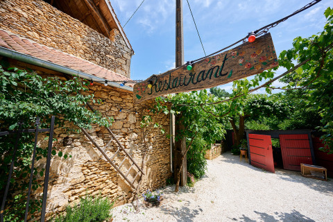 Entrada de restaurante al aire libre con cartel rústico en Camping Le Pech Charmant, Nouvelle-Aquitania, Francia.