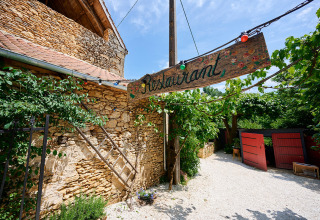 Buiteningang van restaurant met rustiek houten bord bij Camping Le Pech Charmant in Nouvelle-Aquitaine, Frankrijk.