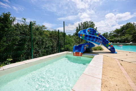 Un tobogán acuático colorido desemboca en la piscina infantil de Camping Le Pech Charmant en Nouvelle-Aquitaine, Francia.