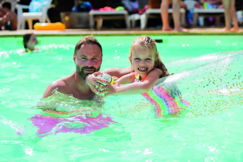 Hombre y niña disfrutan en la piscina con flotador en Camping Le Pech Charmant, Nouvelle-Aquitaine, Francia.
