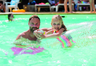 Man and girl smile together in the pool with a float at Camping Le Pech Charmant, Nouvelle-Aquitaine, France.
