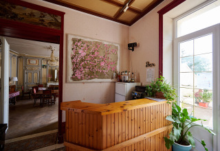 Wooden reception desk with plants and bar area in a holiday park, looking into an elegant dining room.