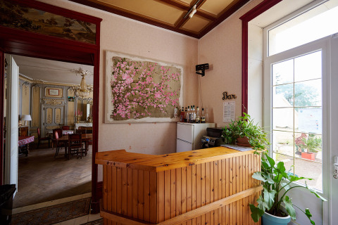 Reception in legno con piante e zona bar in un villaggio vacanze, vista su una sala da pranzo elegante.