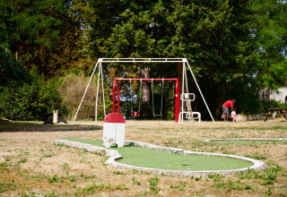 En legeplads med gynger og minigolf i det fri på Camping Le Petit Trianon i Nouvelle-Aquitaine, Frankrig.
