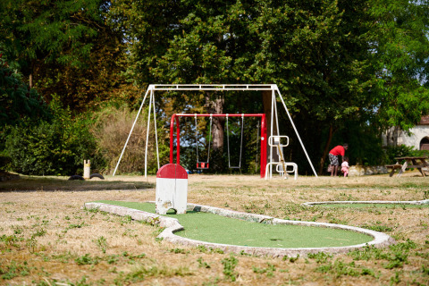 En legeplads med gynger og minigolf i det fri på Camping Le Petit Trianon i Nouvelle-Aquitaine, Frankrig.