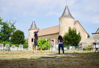 Un uomo e una ragazza giocano a mini golf davanti a un castello al Camping Le Petit Trianon in Nouvelle-Aquitaine, Francia.