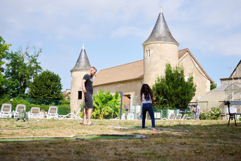 Ein Mann und ein Mädchen spielen Minigolf vor einem Schloss im Camping Le Petit Trianon, Nouvelle-Aquitaine, Frankreich.