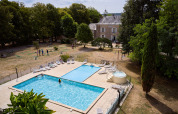 Udsigt over swimmingpool, liggestole og små golfbaner i ferieparken Camping Le Petit Trianon i Frankrig.
