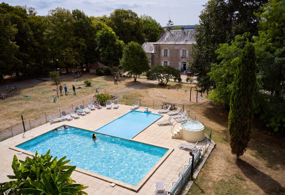 Udsigt over swimmingpool, liggestole og små golfbaner i ferieparken Camping Le Petit Trianon i Frankrig.