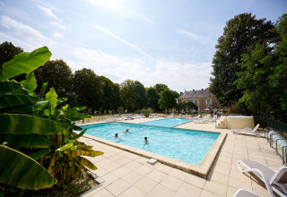 Udendørs swimmingpool med gæster, liggestole og grønne træer på Camping Le Petit Trianon i Frankrig.