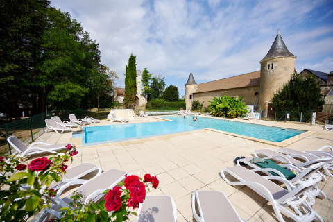 Piscina all'aperto con lettini, fiori e edificio storico a Camping Le Petit Trianon, Nouvelle-Aquitaine, Francia.