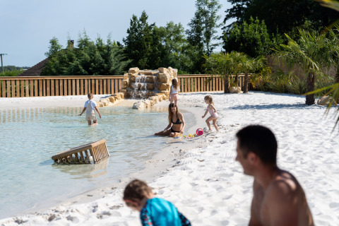 Families enjoying the sandy poolside and sunshine at Camping Le Sequoia in Nouvelle-Aquitaine, France.