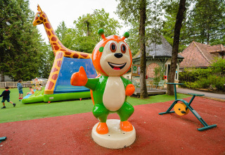 Playground at Camping Le Sequoia in Nouvelle-Aquitaine, France, with colorful mascot statue and children playing.