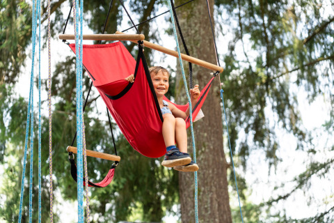 Niño jugando en un columpio rojo al aire libre en Camping Le Sequoia, un parque vacacional en Nouvelle-Aquitaine, Francia.