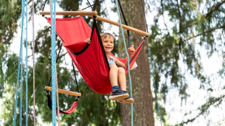 Niño jugando en un columpio rojo al aire libre en Camping Le Sequoia, un parque vacacional en Nouvelle-Aquitaine, Francia.