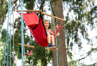 Niño jugando en un columpio rojo al aire libre en Camping Le Sequoia, un parque vacacional en Nouvelle-Aquitaine, Francia.