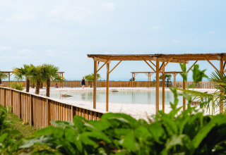Relaxing view of Camping Le Sequoia holiday park in Nouvelle-Aquitaine, France, with pool and palm trees.