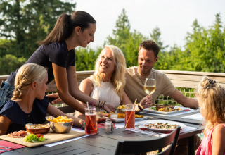 En familie nyder et måltid udendørs på Camping Le Sequoia feriepark i Nouvelle-Aquitaine, Frankrig.