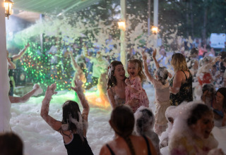 Adults and children play and dance in foam at a lively party at Camping Le Sequoia, Nouvelle-Aquitaine, France.