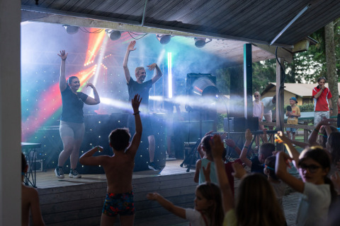 Niños bailando frente a un escenario iluminado en Camping Le Sequoia, parque de vacaciones en Nouvelle-Aquitaine, Francia.