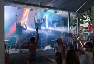 Niños bailando frente a un escenario iluminado en Camping Le Sequoia, parque de vacaciones en Nouvelle-Aquitaine, Francia.