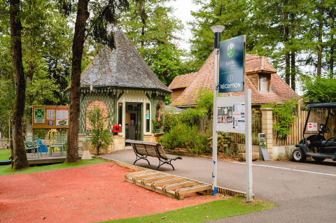Área de recepción del Camping Le Sequoia en Nouvelle-Aquitaine, Francia, rodeada de árboles y bancos.