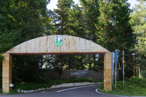 Wooden entrance gate of Camping Le Sequoia holiday park surrounded by green trees in Nouvelle-Aquitaine, France.