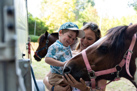 Un niño feliz y su madre acarician un pony en Camping Le Sequoia, un parque de vacaciones en Nouvelle-Aquitaine, Francia.
