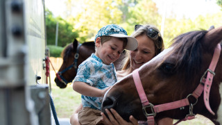 Un niño feliz y su madre acarician un pony en Camping Le Sequoia, un parque de vacaciones en Nouvelle-Aquitaine, Francia.
