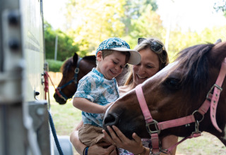 Un niño feliz y su madre acarician un pony en Camping Le Sequoia, un parque de vacaciones en Nouvelle-Aquitaine, Francia.