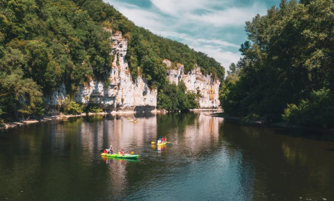 People kayaking on a river at Camping Le Sequoia, surrounded by lush trees and white cliffs in France.