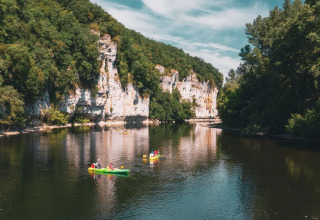 People kayaking on a river at Camping Le Sequoia, surrounded by lush trees and white cliffs in France.