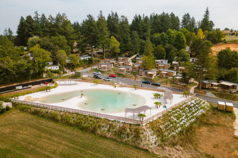 Aerial view of Camping Le Sequoia holiday park with cabins and lagoon surrounded by trees in Nouvelle-Aquitaine, France.