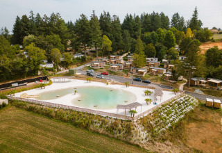 Aerial view of Camping Le Sequoia holiday park with cabins and lagoon surrounded by trees in Nouvelle-Aquitaine, France.