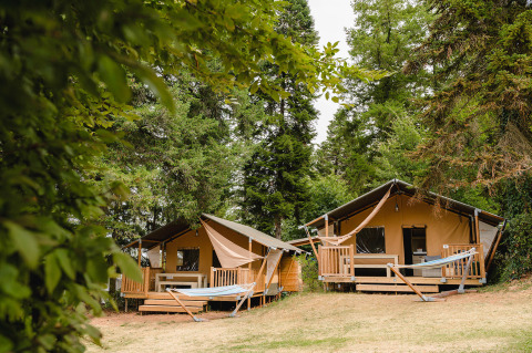 Dos tiendas glamping con terrazas y hamacas en medio del bosque en Camping Le Sequoia, Nouvelle-Aquitania, Francia.