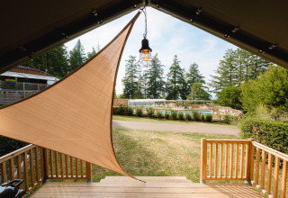 View from a shaded deck looking toward a swimming pool and trees at Camping Le Sequoia, Nouvelle-Aquitaine, France.