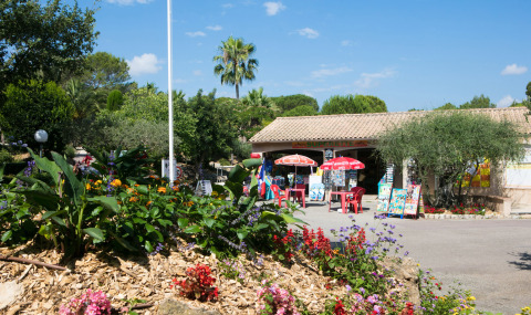 Giardino fiorito e negozio con ombrelloni al Camping Leï Suves, villaggio turistico in Provenza-Alpi-Costa Azzurra, Francia.