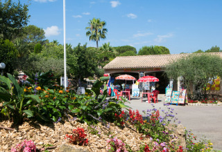 Giardino fiorito e negozio con ombrelloni al Camping Leï Suves, villaggio turistico in Provenza-Alpi-Costa Azzurra, Francia.