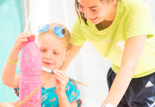 Una bambina dipinge una bottiglia di plastica rosa aiutata da un adulto al Camping Leï Suves in Provenza-Alpi-Costa Azzurra, Francia.