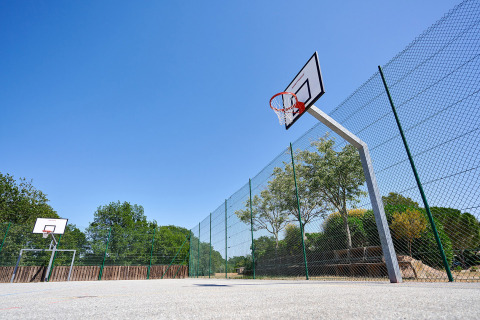 Campo da basket all'aperto con recinzione e cielo blu al Camping Leï Suves in Provenza-Alpi-Costa Azzurra, Francia.