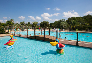 Piscina all’aperto al Camping Leï Suves, con area bambini, animali colorati e palme in Provenza, Francia.