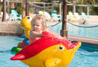 Klein meisje geniet op een kleurrijk vis-speeltoestel in het zwembad bij Camping Leï Suves, Provence, Frankrijk.