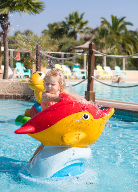 Niña pequeña juega en una figura acuática de pez en la piscina de Camping Leï Suves, en Provenza, Francia.